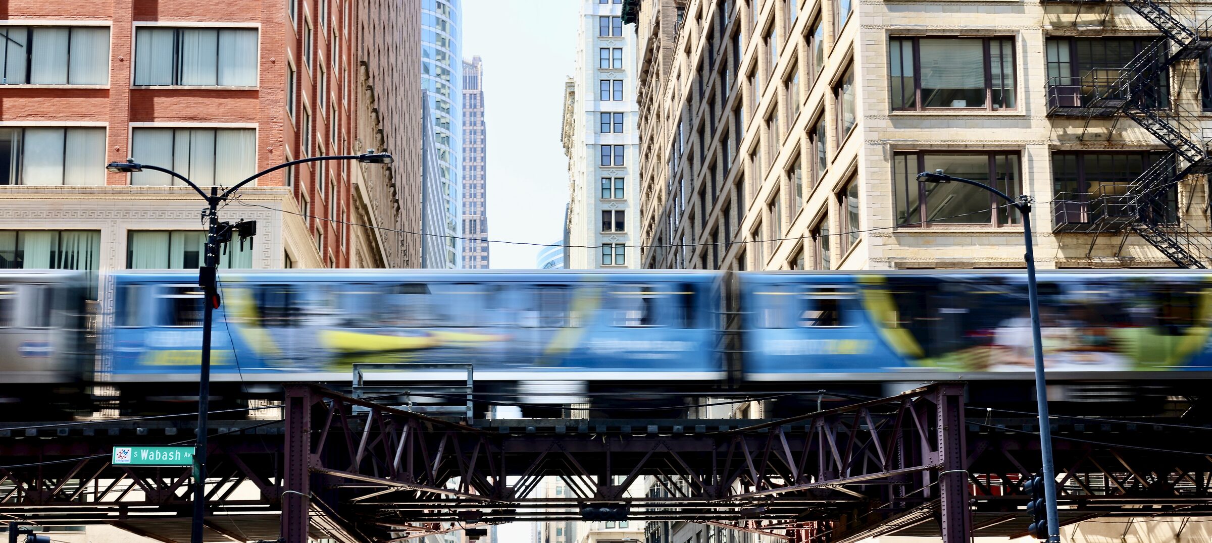 A CTA L train, blurred with motion, crossing the elevated structure above a Loop street lined with buildings